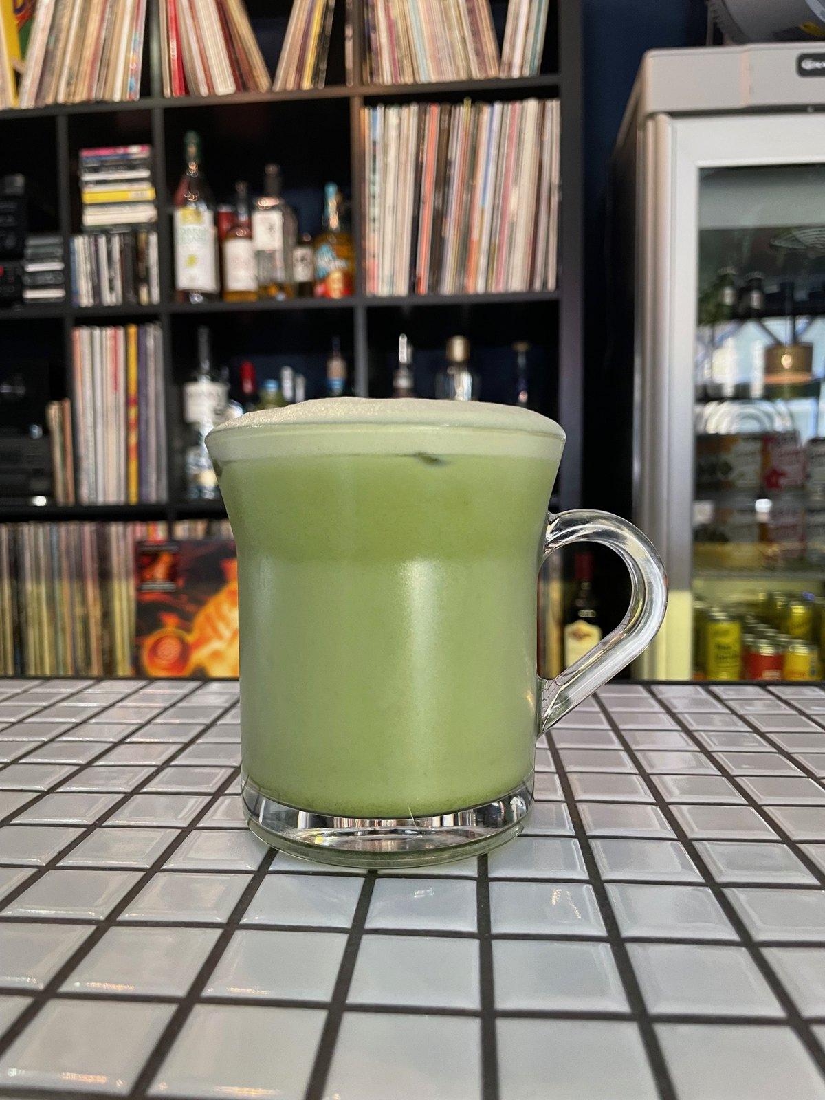 A matcha latte in a glass mug in front of the record shelves